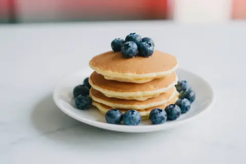 Stos puszystych pancakes z borówkami, ozdobiony świeżymi owocami. Idealne na słodkie śniadanie.