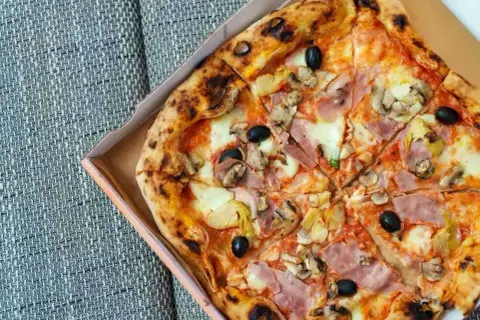 Pyszna pizza capricciosa z szynką, pieczarkami, oliwkami i karczochami, prosto z pieca, w pudełku.