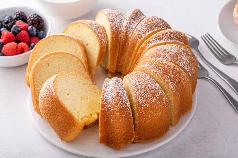 Puszysta babka z cukrem pudrem, idealna na niedzielny deser. Ten przepis na babkę to klasyka. Obok miseczka z owocami leśnymi.