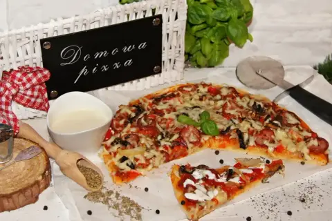 Domowa pizza bez drożdży, z kiełbasą i warzywami, gotowa do podania. Obok sos i przyprawy.
