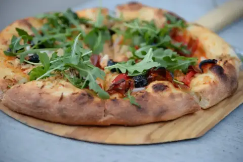 Pyszny, świeżo upieczony spód do pizzy z rukolą, oliwkami i papryką, podany na drewnianej desce.