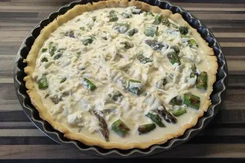 Tarta ze szparagami, gotowa do pieczenia, z kremowym nadzieniem i serem.