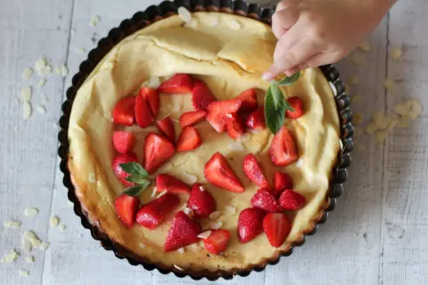 Puszysty dutch baby z truskawkami i płatkami migdałów, dekorowany przez dziecko.