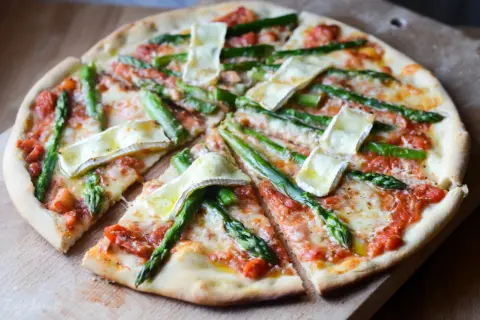 Pyszna pizza ze szparagami i serem brie, polana sosem pomidorowym, pokrojona na kawałki.