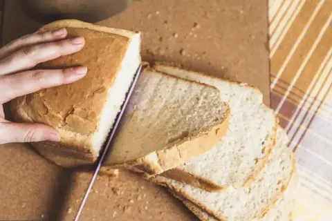 Ręka kroi świeżo upieczony chleb, idealny do każdego posiłku. Ten przepis na chleb jest prosty i pyszny.