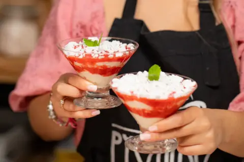 Dwie porcje Eton Mess w kieliszkach, z truskawkami i bitą śmietaną, ozdobione miętą.