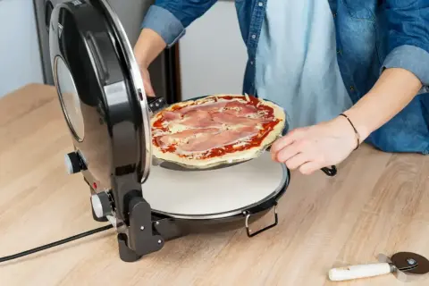 Osoba wkłada pizzę z szynką do pieca. Zobacz, ile piec pizze!