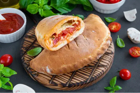 Pyszny calzone przepis: złociste ciasto z sosem pomidorowym i serem, podane z pomidorkami i bazylią.
