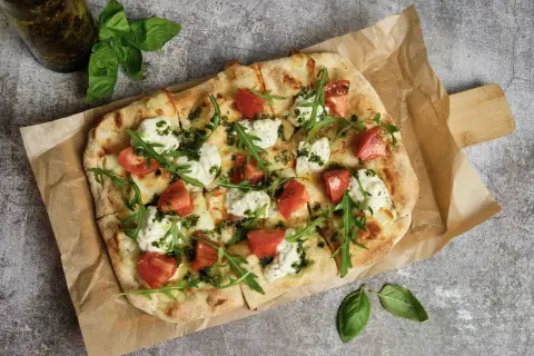 Pyszna pizza z pomidorami, mozzarellą i rukolą. Idealna inspiracja, z czym zrobić pizzę na szybki obiad.