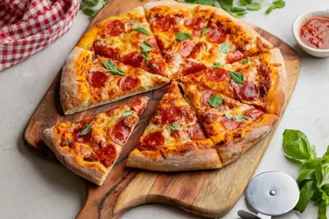 Apetyczna pizza pepperoni z ciągnącym się serem i świeżą bazylią, podana na drewnianej desce.
