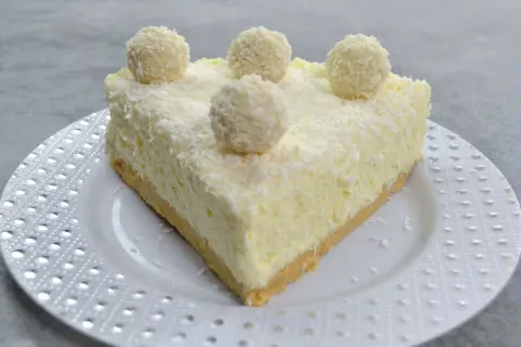 Pyszny sernik Rafaello, udekorowany wiórkami kokosowymi i kulkami przypominającymi Rafaello.