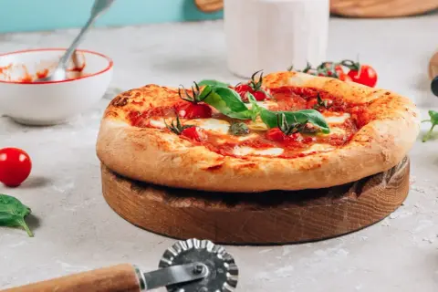 Pyszna pizza na drewnianej desce, gotowa do pokrojenia. Idealna do piekarnika, dzięki kamieniowi do pizzy.