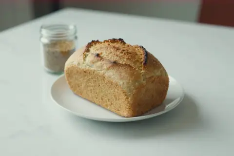Chleb z mąki ryżowej, lekko przypieczony, na białym talerzyku. Obok słoiczek z ziarnami.
