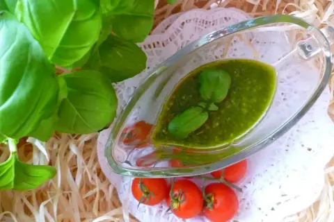 Aromatyczne pesto bazyliowe w sosjerce, ozdobione listkami bazylii, obok gałązki pomidorków koktajlowych.