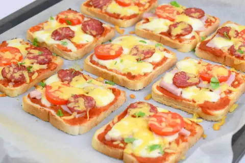 Pyszne pizza z chleba tostowego z serem, salami i pomidorkami, gotowa do pieczenia.