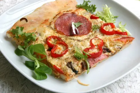 Kawałek pizzy z salami, papryką i serem na białym talerzu. Idealne ciasto na pizzę z chrupiącymi brzegami.