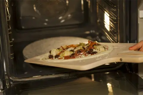 Pizza z dodatkami na łopacie do pizzy, gotowa do wsunięcia na kamień do pizzy granitowy w rozgrzanym piekarniku.