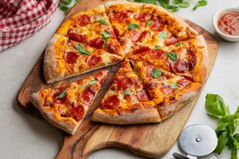Pyszna pizza gourmet z pepperoni, ciągnącym serem i świeżą bazylią, podana na drewnianej desce.