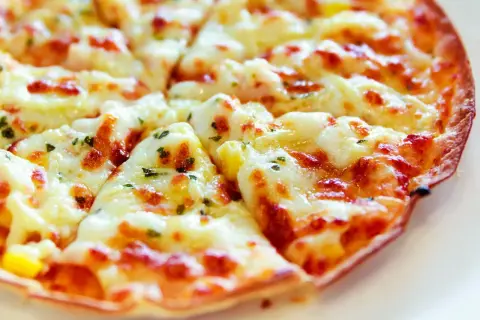 Pyszna pizza z tortilli, obficie posypana serem i ziołami, pokrojona na trójkątne kawałki.