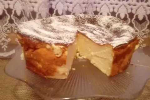 Puszysty sernik z mlekiem skondensowanym, oprószony cukrem pudrem, prezentuje się apetycznie na szklanej paterze.