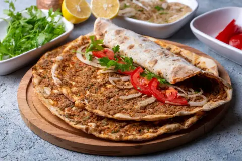 Pyszny lahmacun przepis na cienkim cieście z mięsem mielonym, pomidorami i cebulą. Obok świeża natka, cytryny i pikantne papryczki.