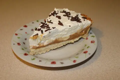 Pyszna tarta bananowa z bitą śmietaną i czekoladową posypką, podana na talerzyku w kwiatki.