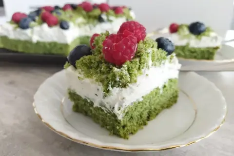 Zielony tort z bitą śmietaną i owocami leśnymi, przypominający leśny mech.
