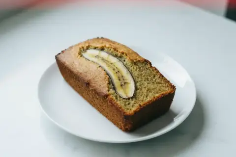Pyszny chlebek bananowy z plasterkiem banana na wierzchu, podany na białym talerzyku.
