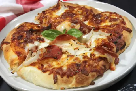 Pyszna pizza z air fryera, z ciągnącym się serem, pepperoni i cebulą, ozdobiona listkiem bazylii.